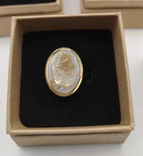 Gold oval ring with white and gold stone displayed in a beige box with black velvet cushion