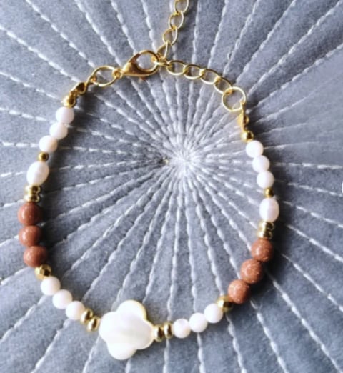 Beaded bracelet with gold chain clasp featuring white, terracotta, and white flower bead on textured gray background